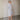 A woman wearing a blue and white vertically striped midi shirt dress, photographed from behind in a minimalist room with a beige wall and concrete floor.