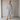 A woman wearing a loose, short-sleeve button-front dress with vertical gray and white stripes, standing in a minimalist gray room.