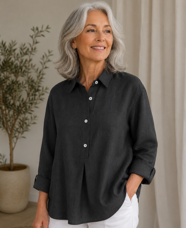 Woman wearing a black shirt and white pants standing indoors with a plant in the background