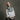 A woman with gray hair wearing a white linen shirt and a slate blue gradient scarf, standing against a textured dark gray studio background.
