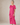 A woman modeling a short-sleeved, loose-fitting midi dress in a vibrant pink fabric against a neutral gray studio background.