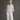 An older woman stands barefoot against a textured gray studio backdrop, wearing a light sage green linen button-up shirt and matching wide-leg linen pants.