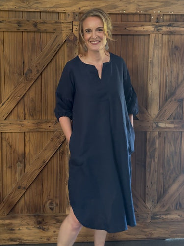 Woman wearing a navy blue dress standing in front of a wooden door.