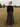 Woman standing in a field wearing a black top and brown wide-leg pants.