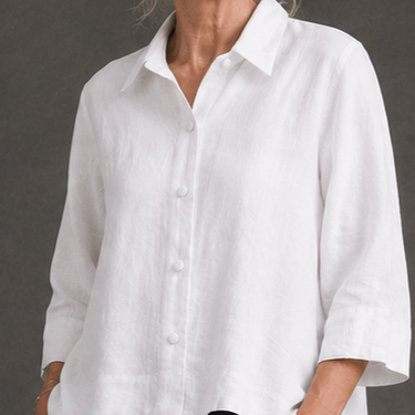 A woman wearing a white long-sleeve linen button-up shirt with a relaxed fit, shown from the neck down against a dark gray background.