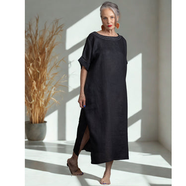 Woman in a black dress standing in a sunlit room with a plant in the background