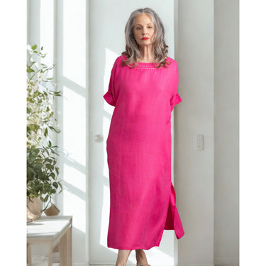Woman wearing a bright pink dress standing in a well-lit room with a plant.