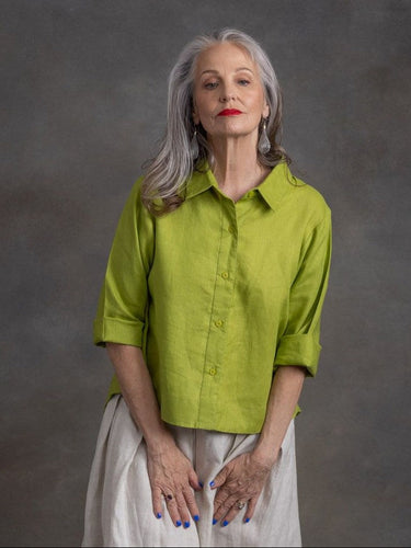 Woman wearing a green shirt and white pants against a gray background