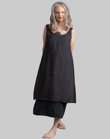 Woman wearing a black sleeveless dress standing in a sunlit room with shadows on the wall.